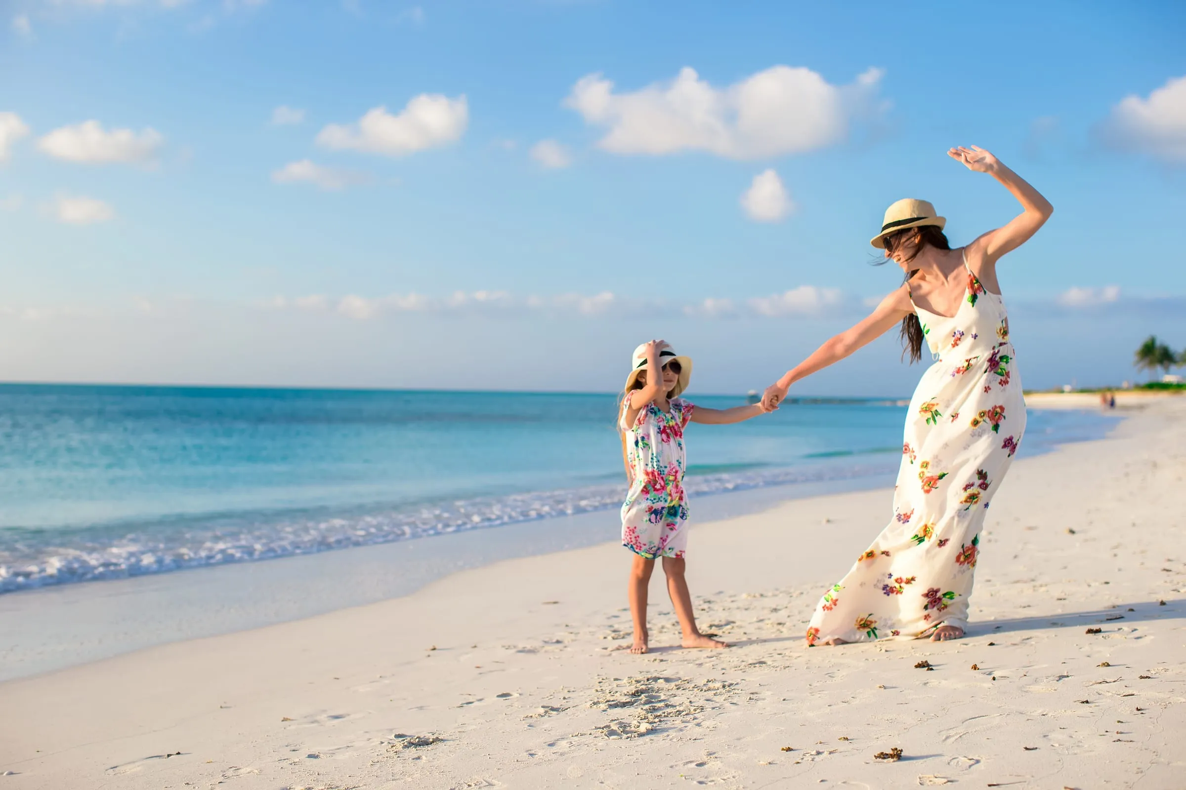 Madre e hija bailando descalzas en una playa de arena blanca