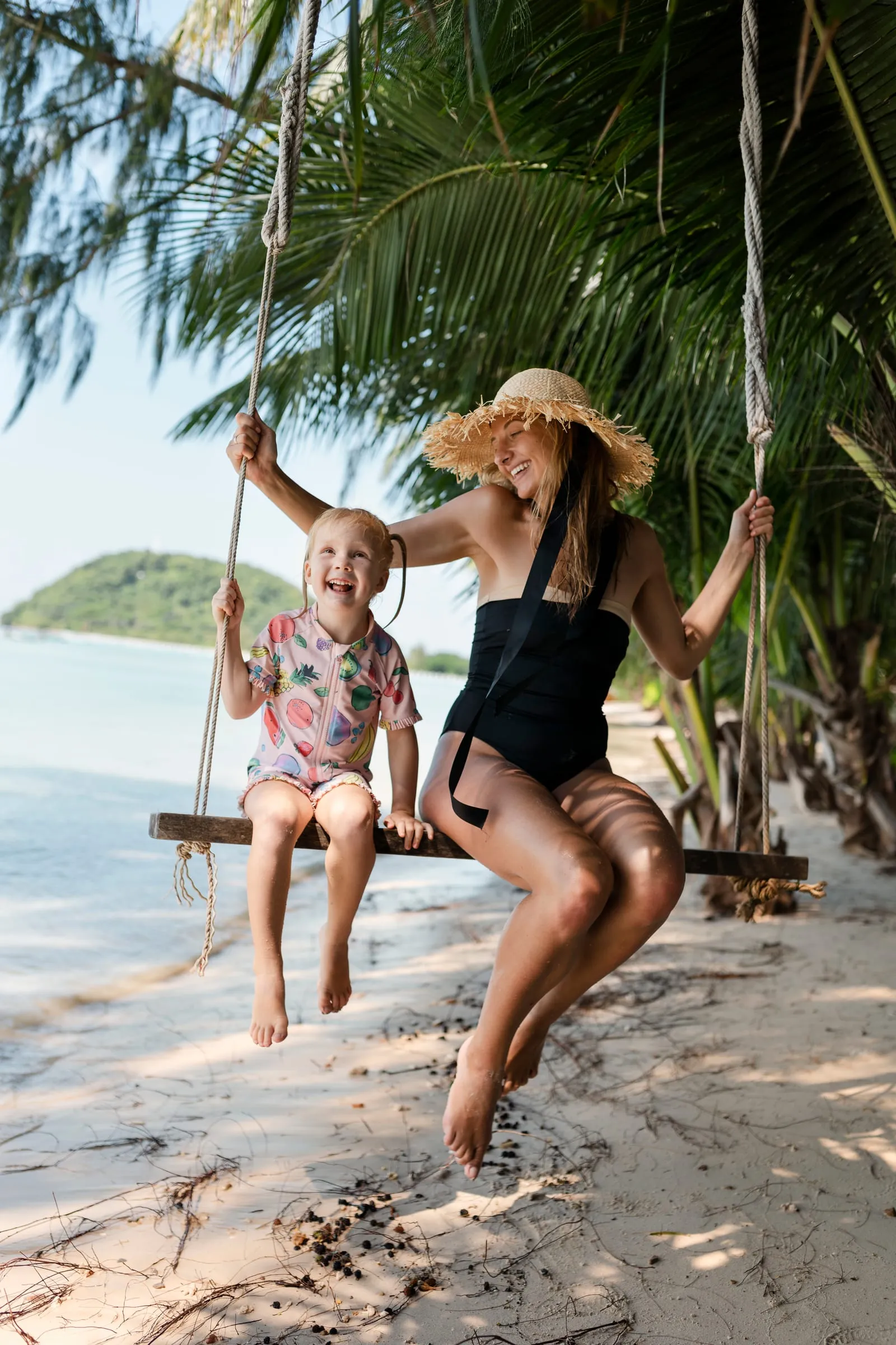 Madre e hija sonriendo en un columpio de cuerda entre palmeras